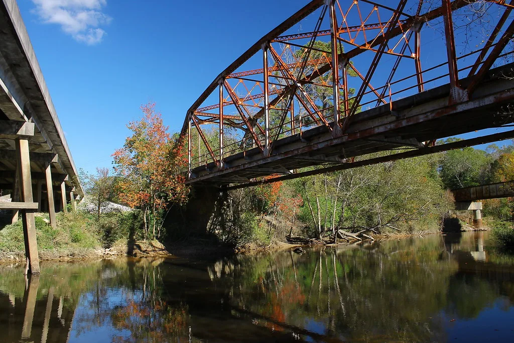 Old rusty metal bridge overgrown with trees above a river.
