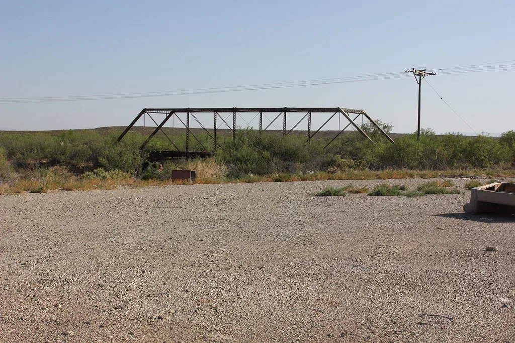 Old metal truss bridge overgrown with shrubs.