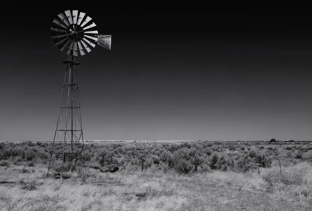 Isolated metal windmill at Kent Homestead in grassland, in black and white.
