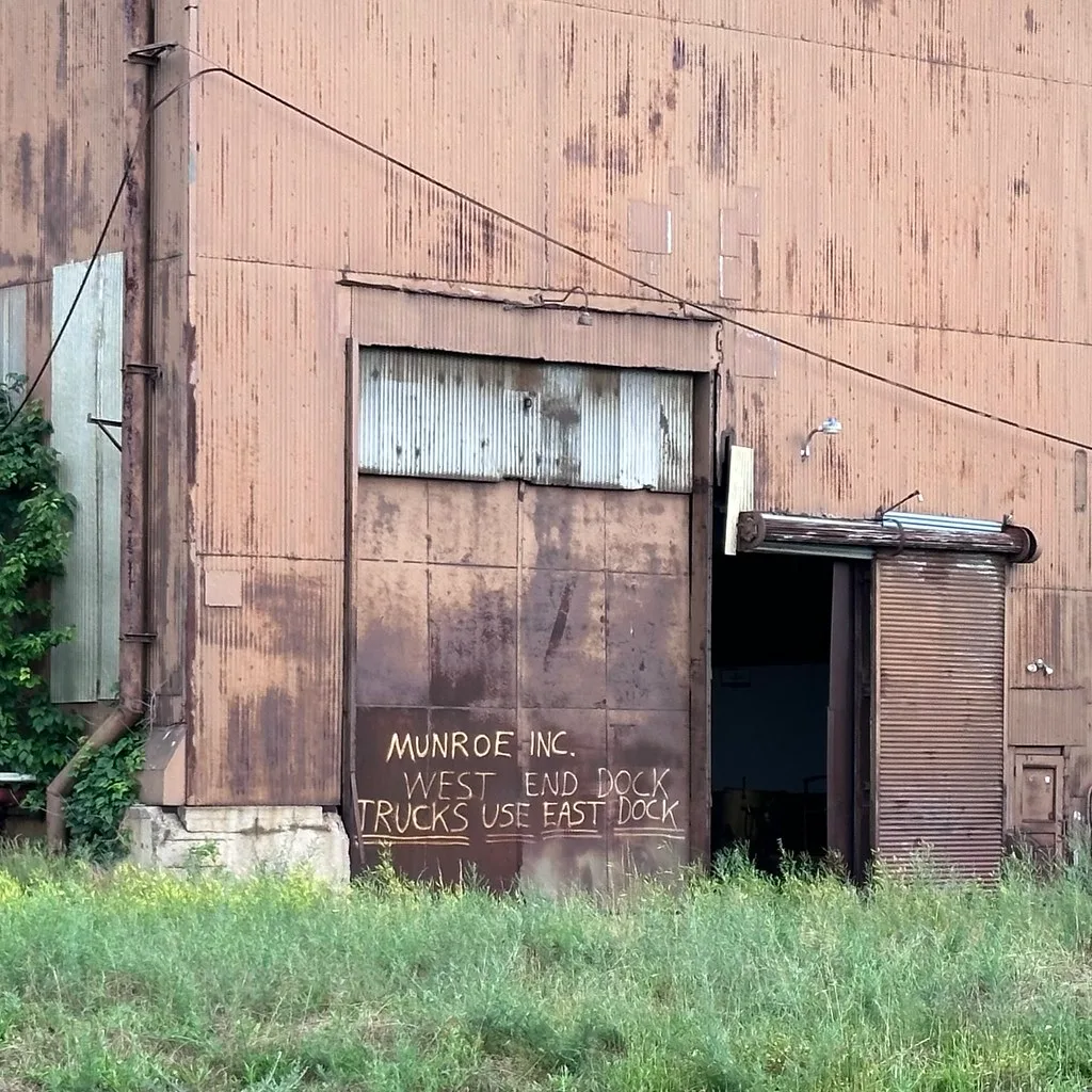 Anciennes portes de quai industriel rouillées devant de hautes herbes.