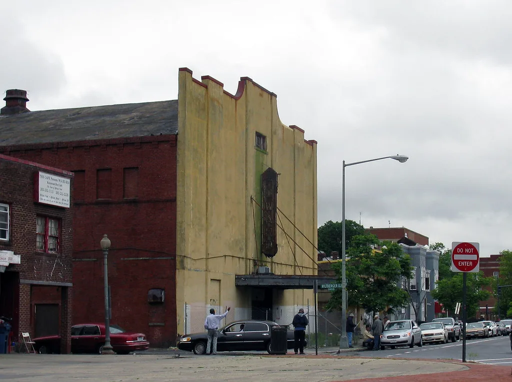 Ancien cinéma délaissé à façade jaune tachée et enseigne verticale rouillée dans une rue urbaine.