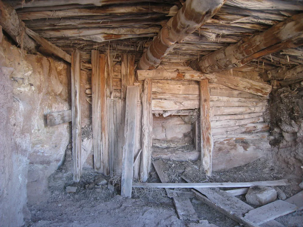 Intérieur de cabane de rondins et de terre avec poutres vieillies et planches tombées au sol.