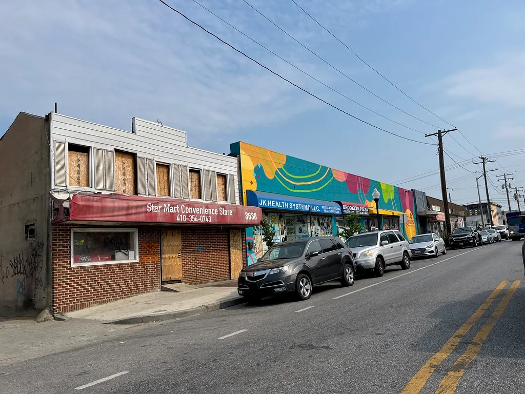 Old boarded storefront beside colorful commercial facades.