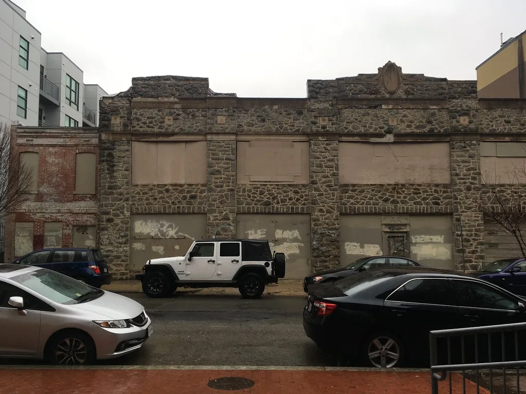 Old stone building with boarded openings behind cars.
