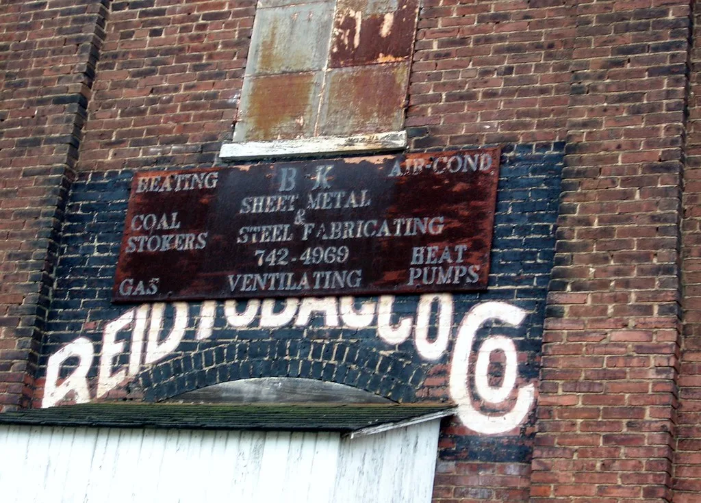 Old workshop sign on a brick facade with sealed openings.