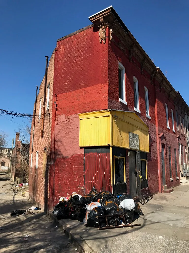 Old red shop with a yellow frontage and rubbish outside the closed entrance.