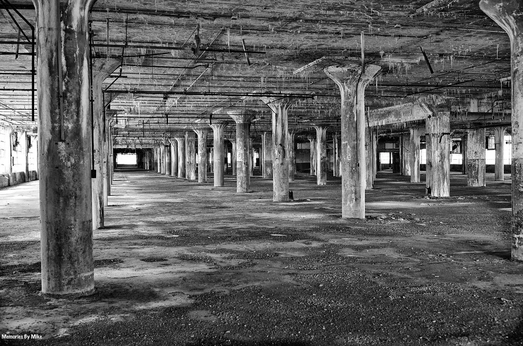 Intérieur industriel vide aux rangées de piliers dégradés, en noir et blanc.