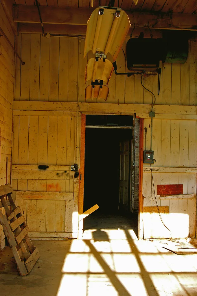 Abandoned workshop with yellow wooden walls and a detached hanging light fixture.