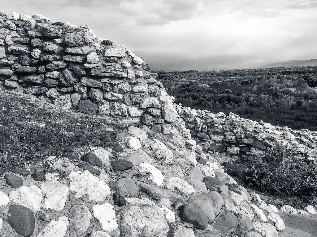 Abandoned stone wall remains and piles of blocks on a rise overlooking the valley, in black and white.