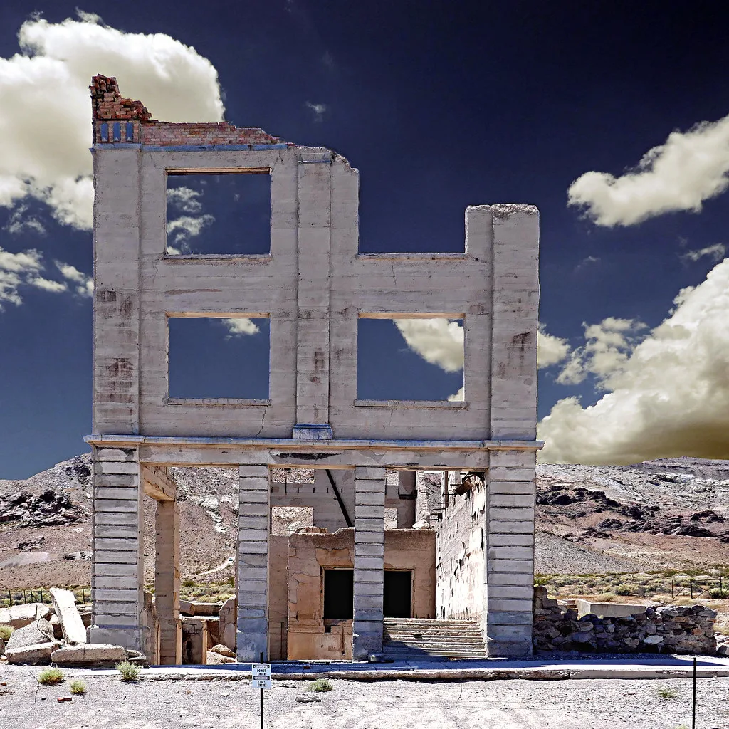 Façade d’un immeuble ruiné à trois niveaux de baies vides dans un paysage désertique.