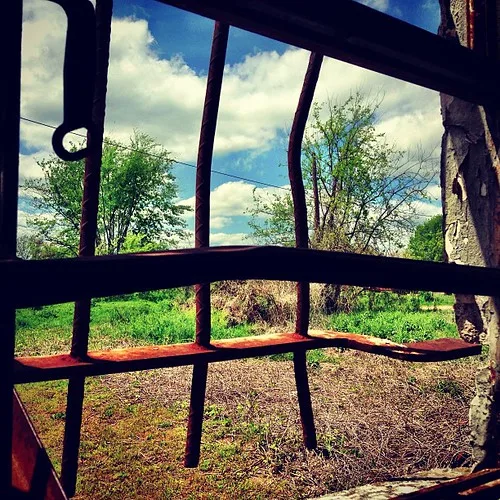 View through an opening with rusted bent bars toward a meadow.