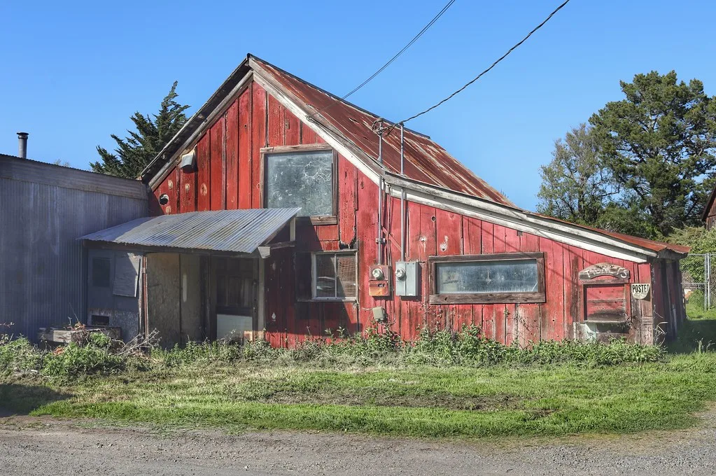 Old red barn with deteriorated cladding surrounded by grass.