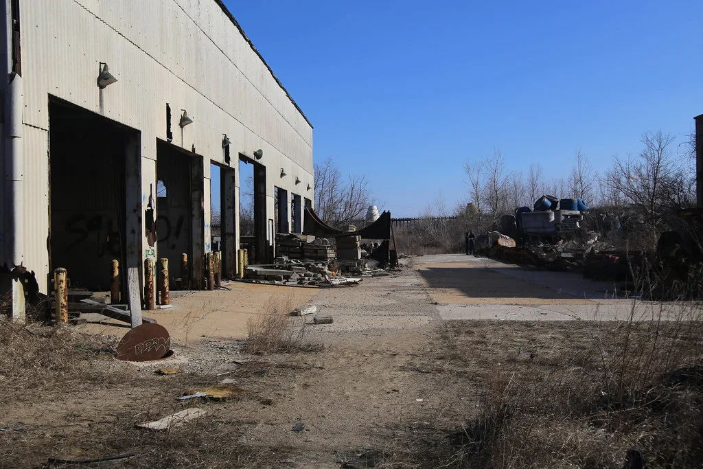 Old hall with missing large doors beside a yard cluttered with debris.