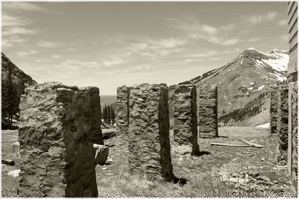 Alignement de piliers de pierre en ruine devant un paysage de montagne enneigée.