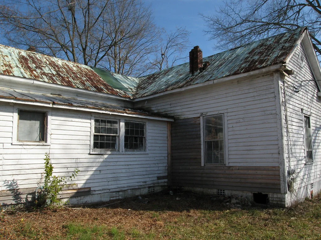 Old white wooden house with broken windows and a rusty roof.