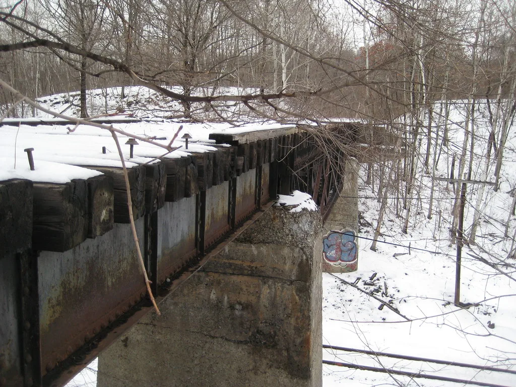 Old metal bridge with snow-covered sleepers in woodland.