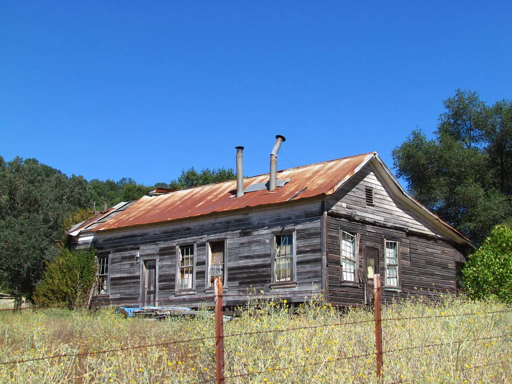 Old wooden house with a rusty roof behind a fence.
