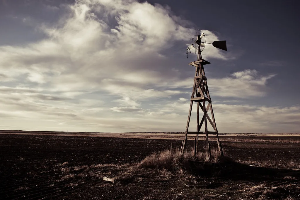 Old wind pump with a damaged rotor on a wooden frame in a field.