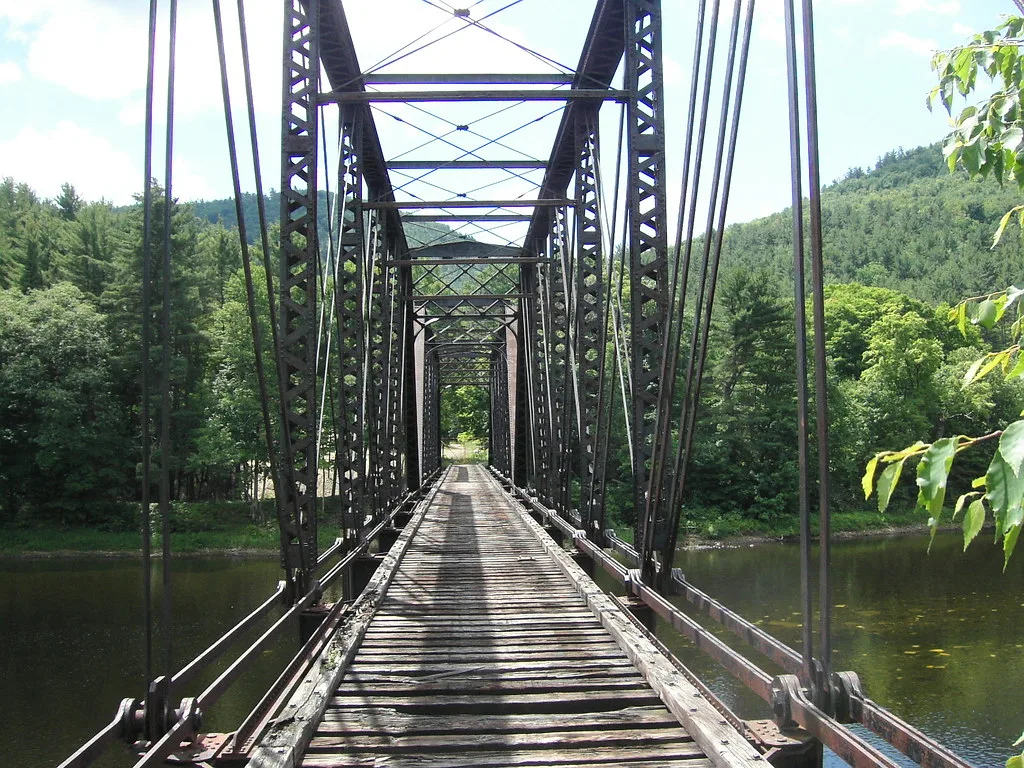 Ancien pont métallique aux traverses de bois dégradées au-dessus de l’eau.