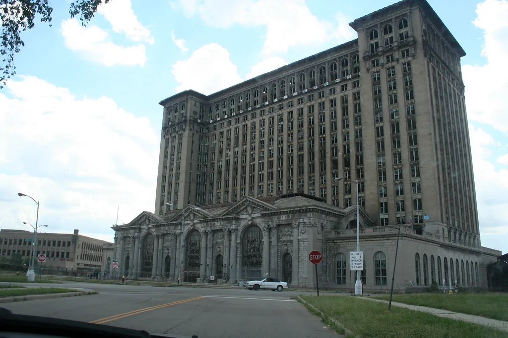 Ancienne gare monumentale abandonnée aux hautes façades percées de fenêtres brisées.