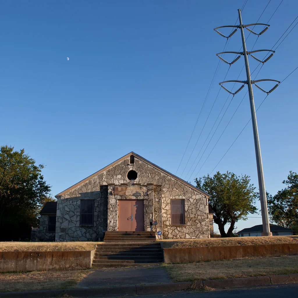 Small stone building sealed with panels, with an empty round opening above the door.