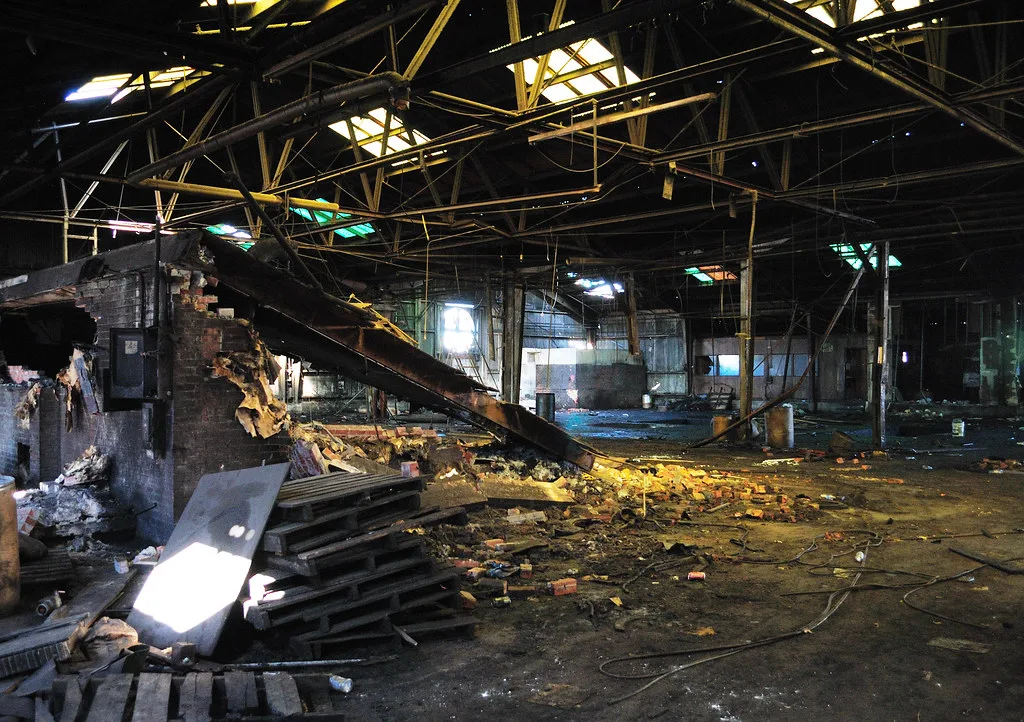 Intérieur d’une ancienne halle industrielle avec gravats et toiture trouée.