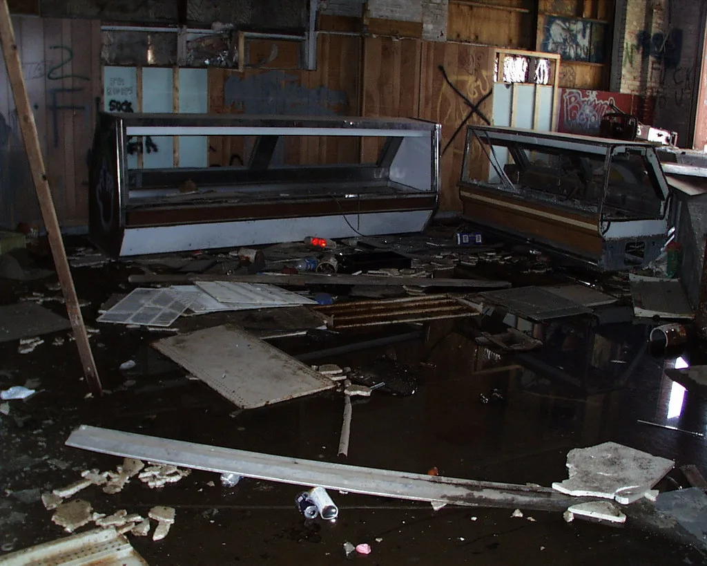 Interior of an abandoned shop with two broken display counters and a flooded floor strewn with panels and debris.