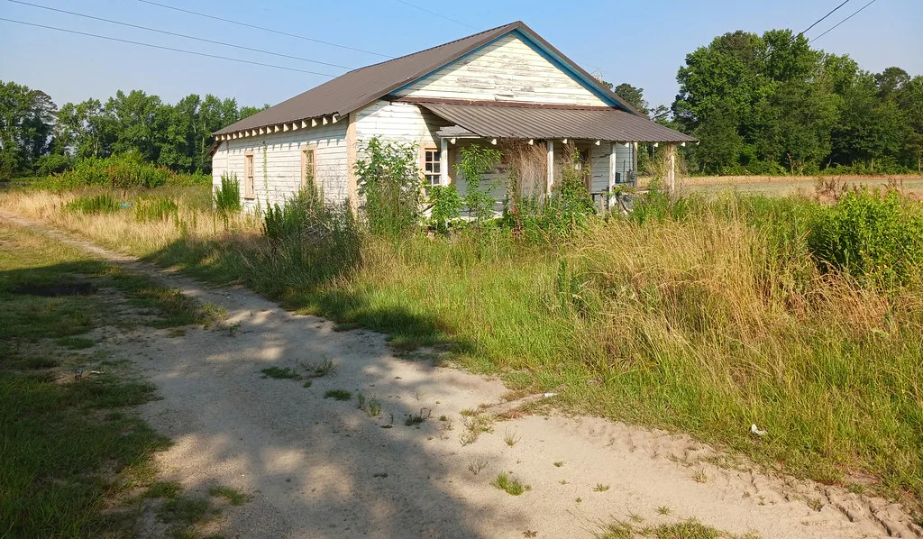 Old white wooden house with tall grass around its porch.