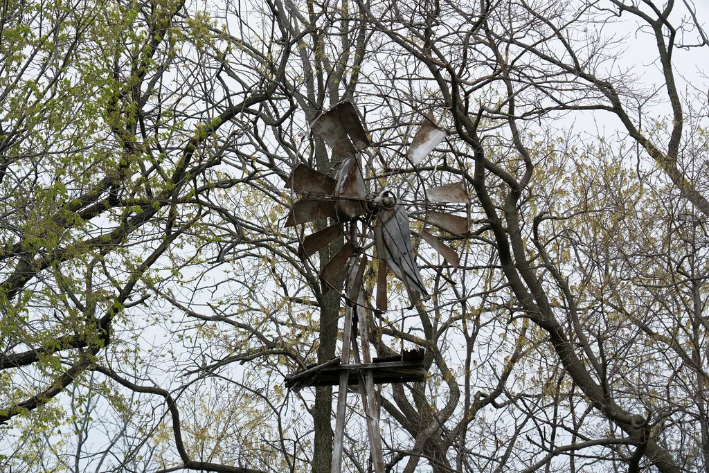 Old windmill with bent metal blades among tree branches.