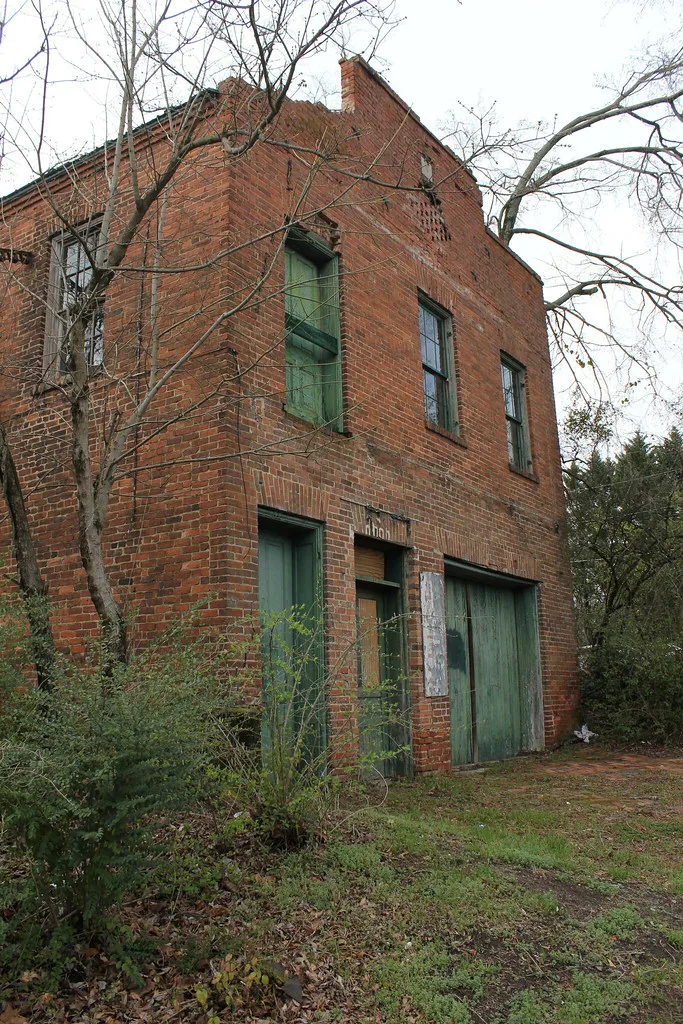 Old brick building with deteriorated green doors among trees.
