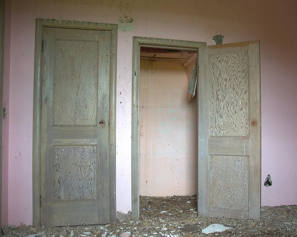Two doors with peeling paint in an abandoned interior strewn with debris.