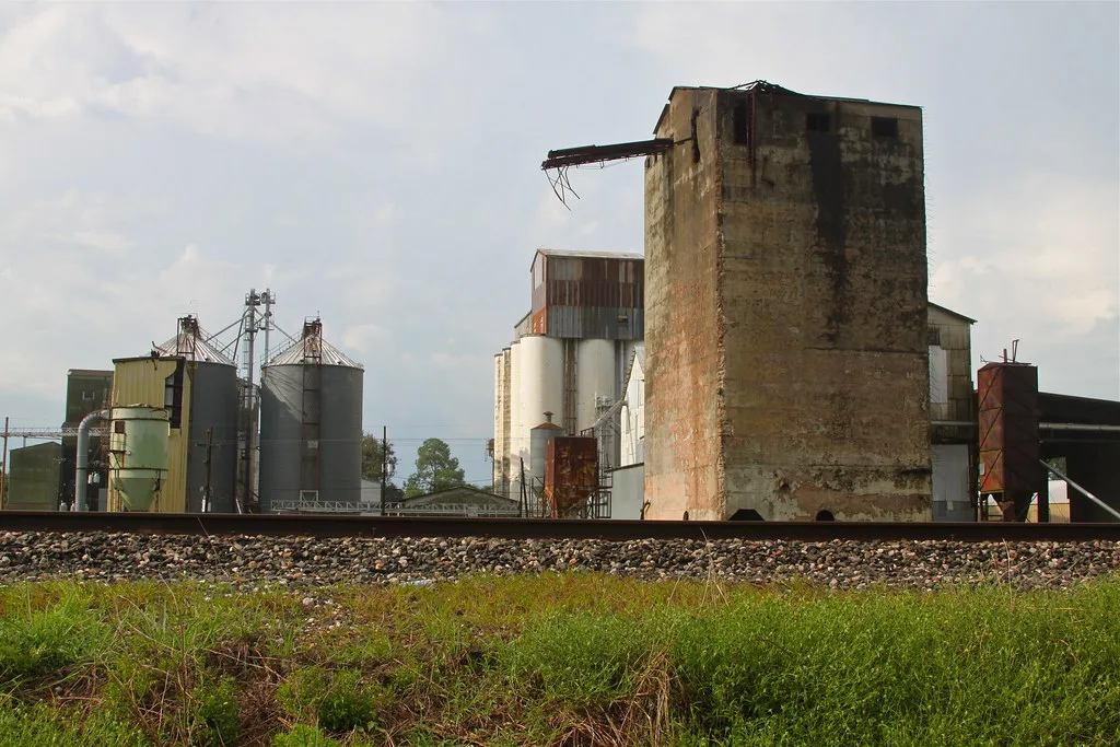 Deteriorated old industrial tower in front of silos and a railway track.