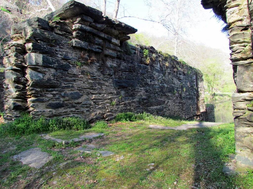 Ruines de pierre d’un bâtiment sans toiture avec haut mur irrégulier et sol herbeux au bord de l’eau.