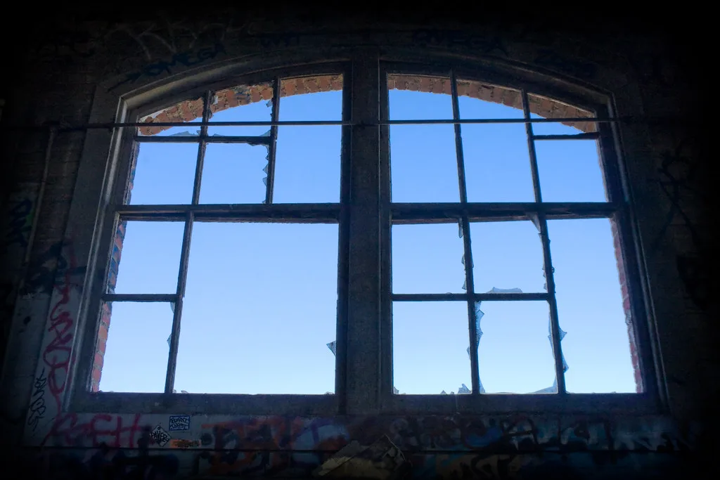 Fenêtre cintrée aux vitres brisées dans un intérieur de brique couvert de graffitis.