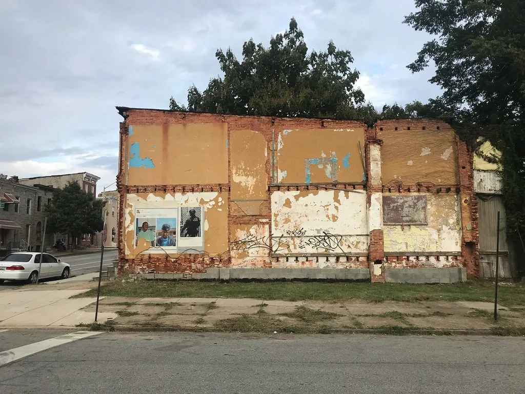 Remaining brick wall of a demolished house with exposed ochre interior plaster on a vacant plot.