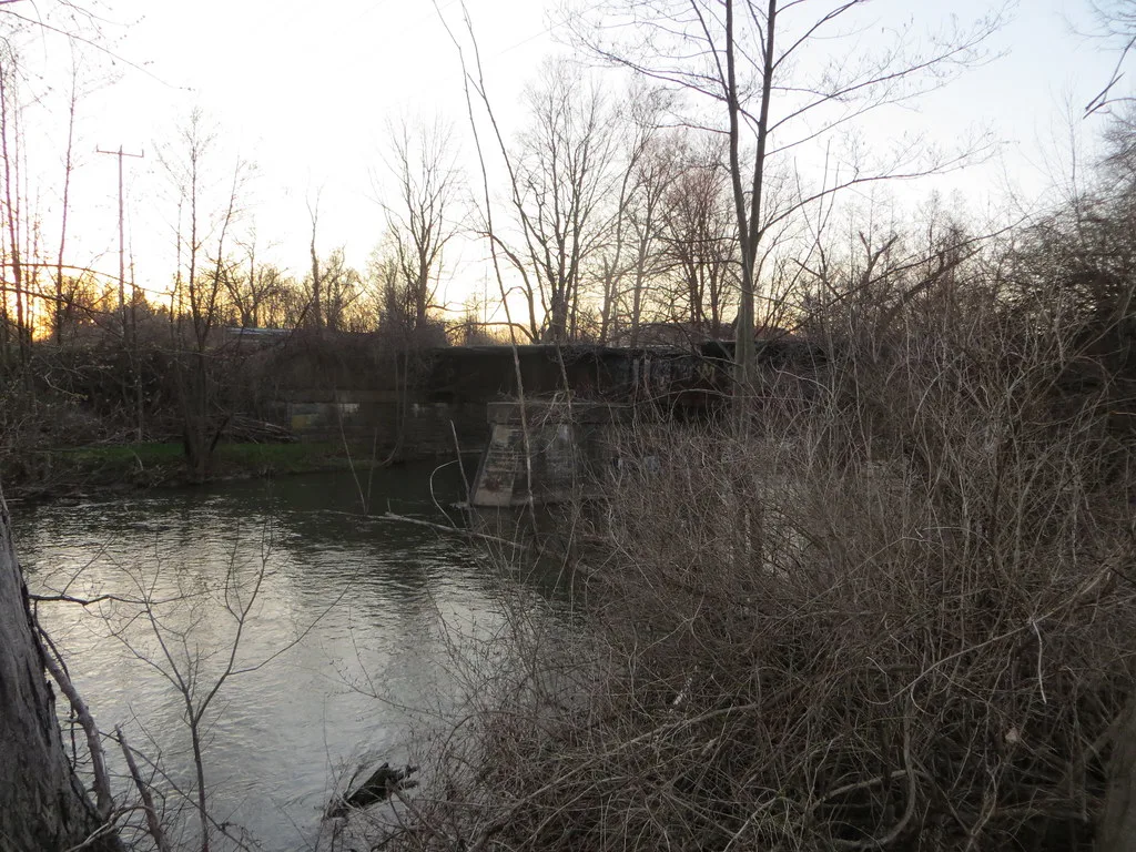 Old bridge on stone piers behind leafless trees.