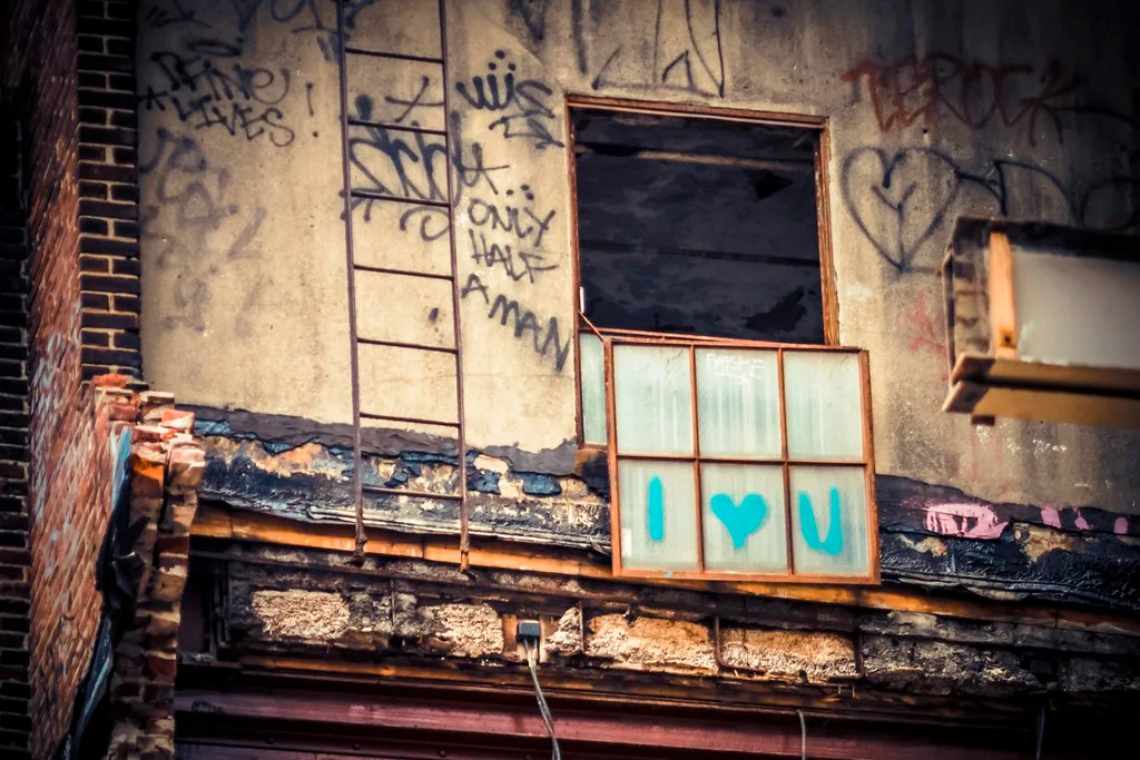 Ruined industrial facade with a partly detached graffiti-covered window.