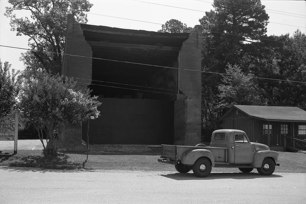 Brick building with its facade missing and broken side walls, photographed in black and white.