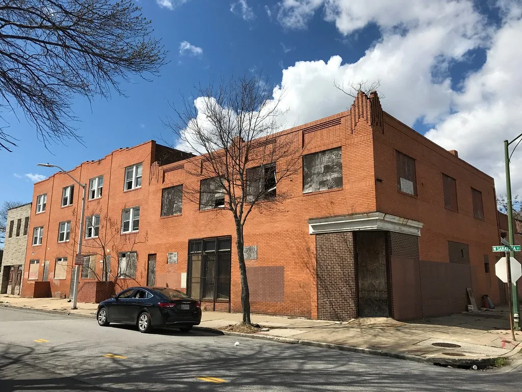 Orange brick corner building with boarded openings.