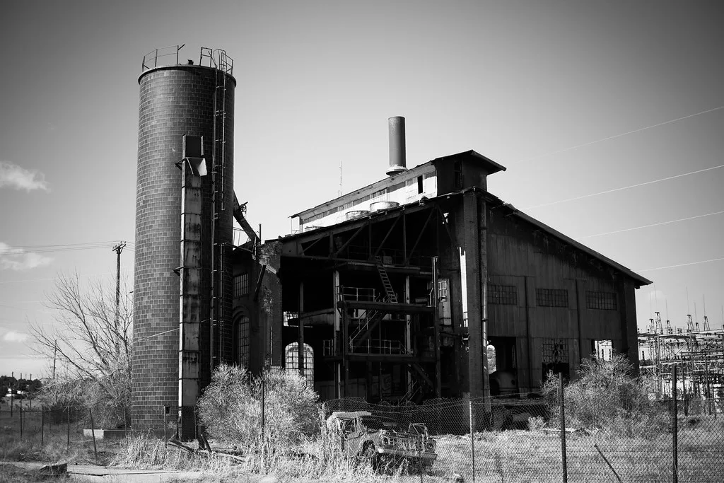 Dilapidated old industrial building and cylindrical tower behind a fence.