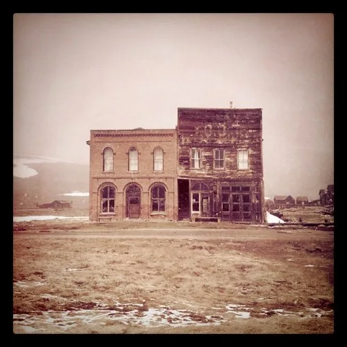 Two isolated old facades, one brick and one deteriorated timber, on bare ground.
