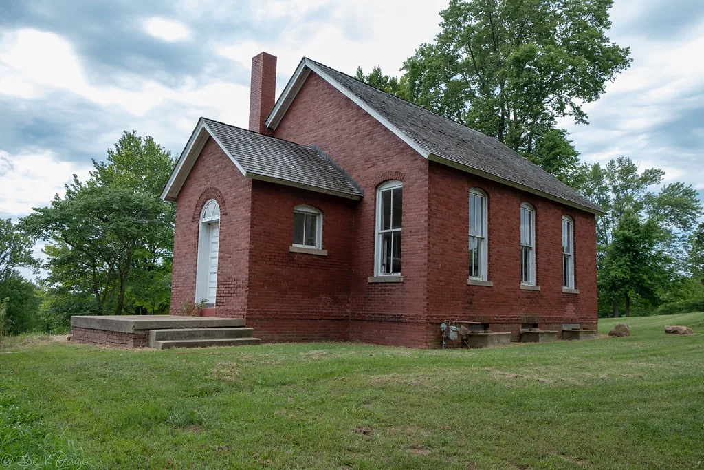 Ancienne école en brique rouge entourée d’herbe.