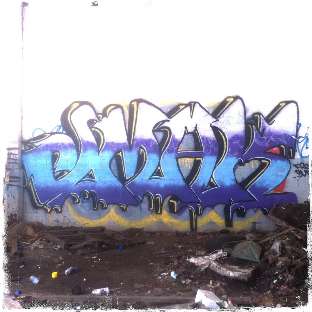 Graffiti-covered wall above a debris-strewn floor in a deteriorated interior.