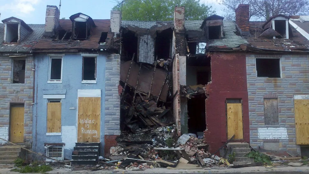 Row of abandoned houses with empty windows and boarded entrances, with a collapsed dwelling in the centre.