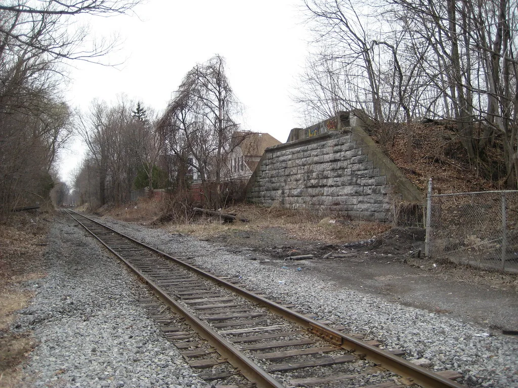 Old stone bridge abutment bordered by trees beside a railway track.