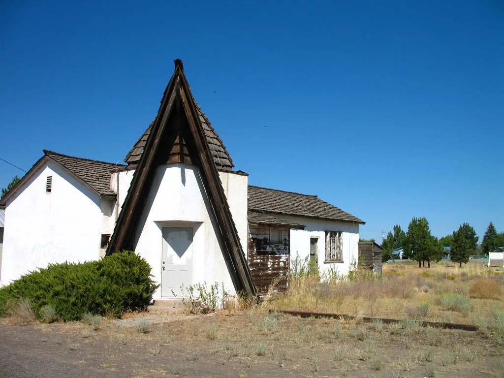 Old white building with a pointed porch surrounded by dry grass.