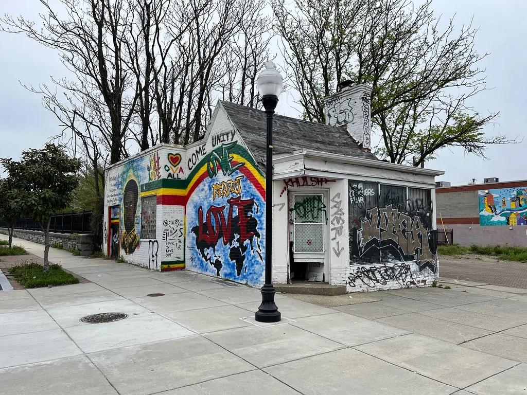 Closed small building with murals and graffiti covering its facades.