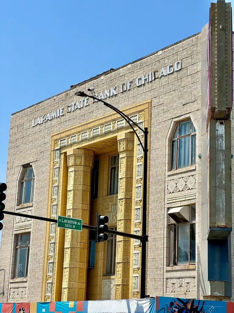Old bank building with a yellow entrance and damaged windows.