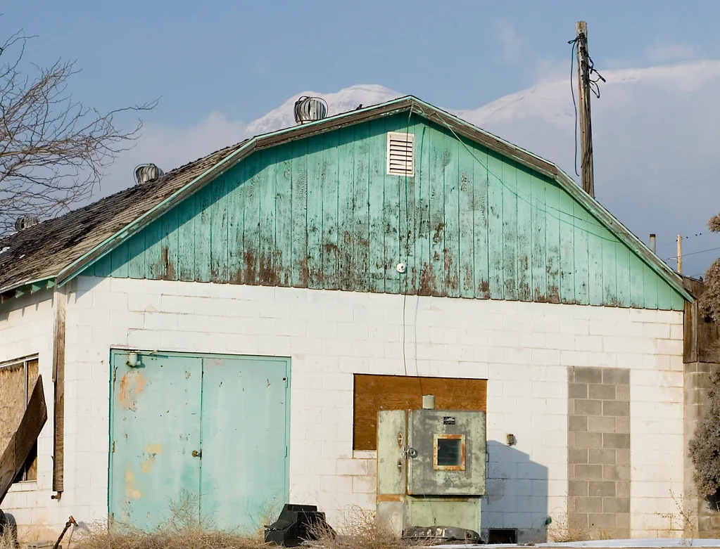 Old white building with a faded green gable and boarded openings.