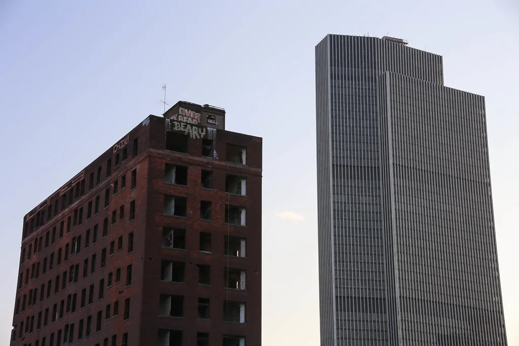 Brick building with empty window openings beside a modern tower.